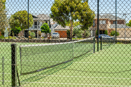 A public tennis court enclosed by a chain-link fence in a residential neighborhood in Australia surrounded by houses and homes. An outdoor sports facility and community amenity. Tarneit, Melbourne