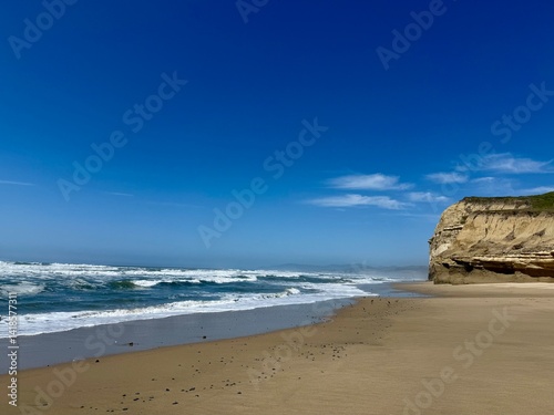 Waves crash along a Northern California coastline under a vibrant blue sky.
