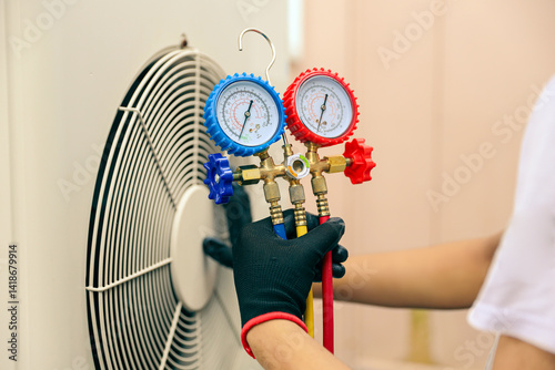 Conditioning technician using manifold gauge measuring tool checking refrigerant pump filling home air conditioner and maintenance heat fix repair and clean outdoor air compressor unit.