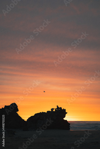 Silhouette of a person sitting on a rock at the beach during a beautiful orange sunrise.