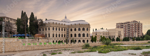 Mahsati Ganjavi Center stands majestically in Ganja, Azerbaijan, highlighted by its distinct domes against a backdrop of a dusky sky. The surrounding area features lush greenery and modern buildings