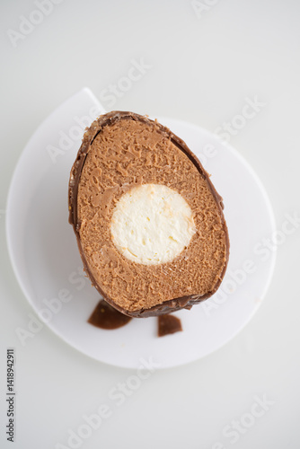 Cross-Section of chocolate and nutty mousse egg with white chocolate ganache creamy center. Easter sweets and treats. Neutral white background with copy space.