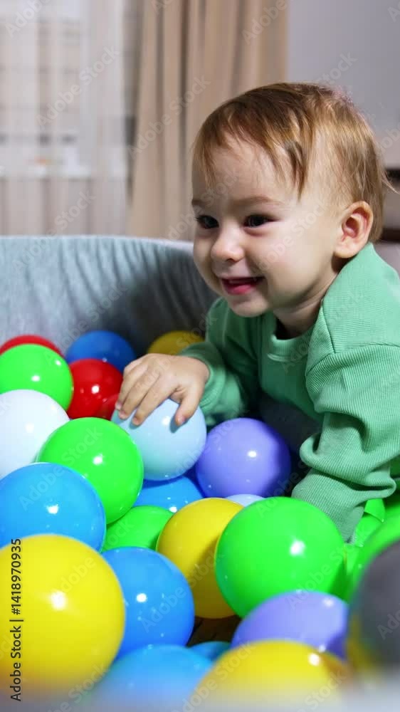 One year old toddler in basin with colourful plastic balls. Sweet pretty kid playing with balls. Vertical video One year old toddler in basin with colourful plastic balls. Sweet pretty kid playing with balls. Vertical video