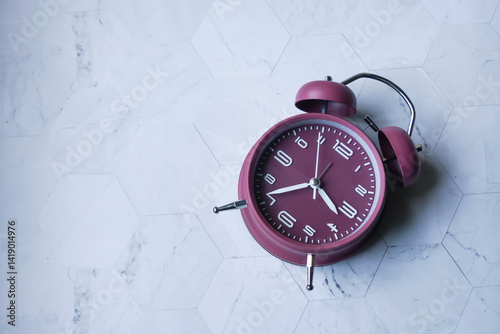 A maroon analog alarm clock with silver legs and twin bells, isolated on white background. 