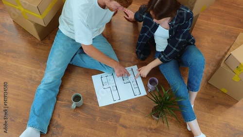 Cheerful man and woman sitting on the floor in new house with coffee and home project discussing interior design and reconstruction. Family moving in new home. Top view. Slow motion