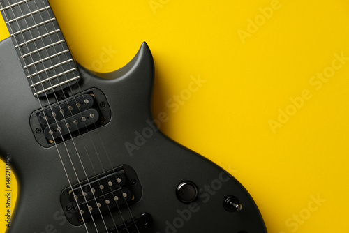 Top view close-up of a matte black electric guitar against a vibrant yellow background. High contrast music concept.