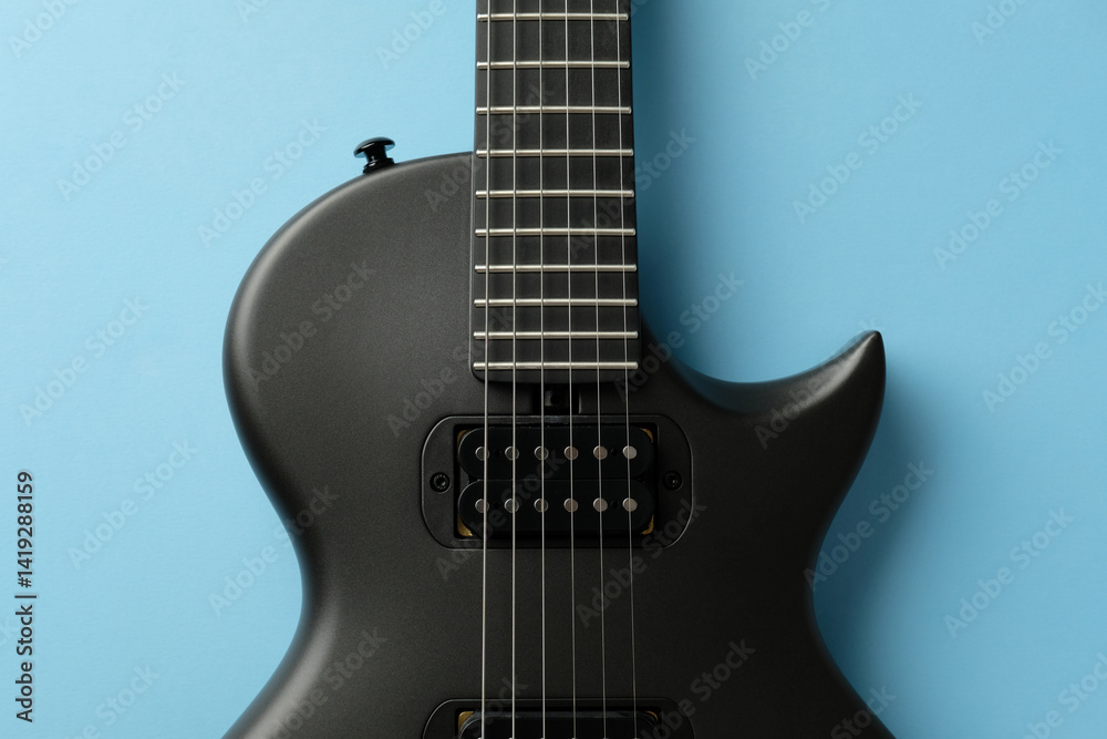 Obraz premium Sleek black electric guitar close-up on a light blue background. Studio shot, perfect for music, rock, instrument, and band related concepts.