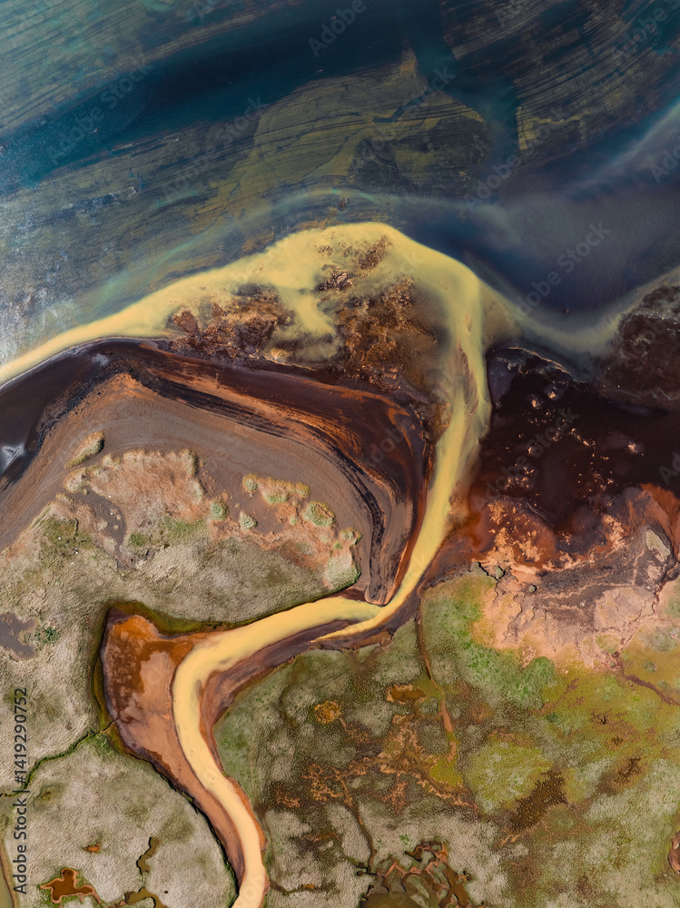 Abstract aerial of a delta where yellow and black sediments meet the deep blue sea, forming organic shapes and colorful contrasts in the coastal wetland.