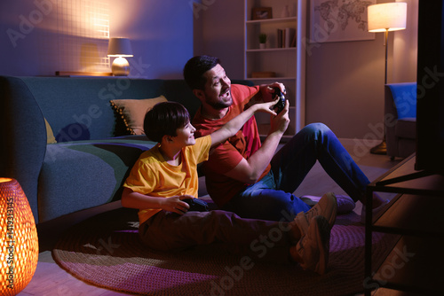 Happy father and his son playing video games on floor in living room at night
