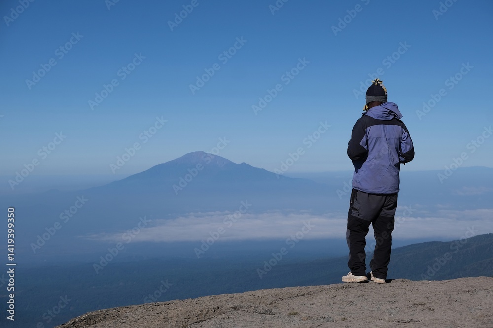 Kilimanjaro, Tanzania: Man standing on viewpoint with Mount Meru on horizon, on trail from Barranco Hut to Barafu Camp, during trekking to Kilimanjaro Peak, Machame Route.