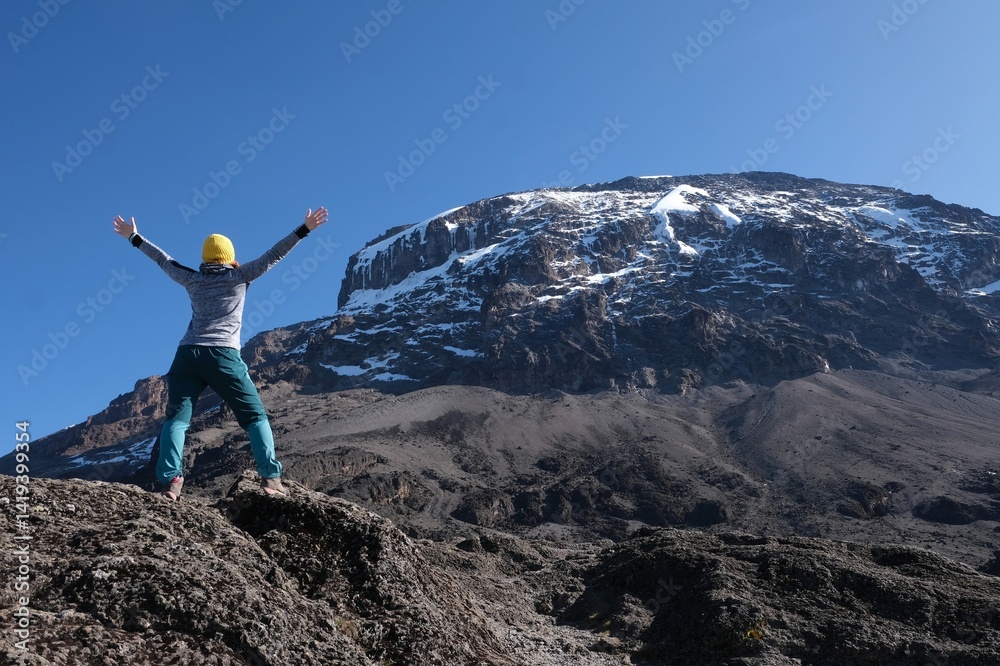 Woman standing with raised hands against peak of Kilimanjaro, on trail from Barranco Hut to Barafu Camp, during trekking to Kilimanjaro Peak, Machame Route. Tanzania