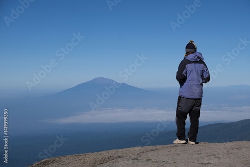 Obraz na płótnie Kilimanjaro, Tanzania: Man standing on viewpoint with Mount Meru on horizon, on trail from Barranco Hut to Barafu Camp, during trekking to Kilimanjaro Peak, Machame Route. w salonie