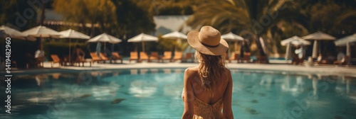 Beautiful young woman with long wavy hair in a straw hat is standing near the swimming pool. Vacation concept. Travel concept, Summertime concept with copy space.