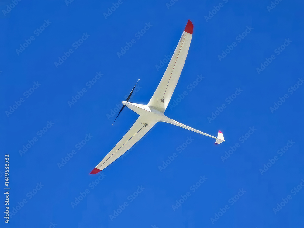 A white and red plane is flying in the sky. The plane is very large and has a red tail. The sky is clear and blue, and the plane is the only object in the sky