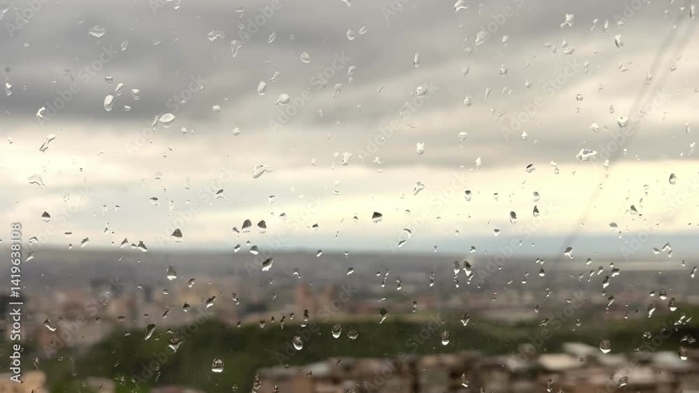 Raindrops on a plastic window with a view of an evening city with a green park and a view of dark gray clouds in slow motion Raindrops on a plastic window with a view of an evening city with a green park and a view of dark gray clouds in slow motion