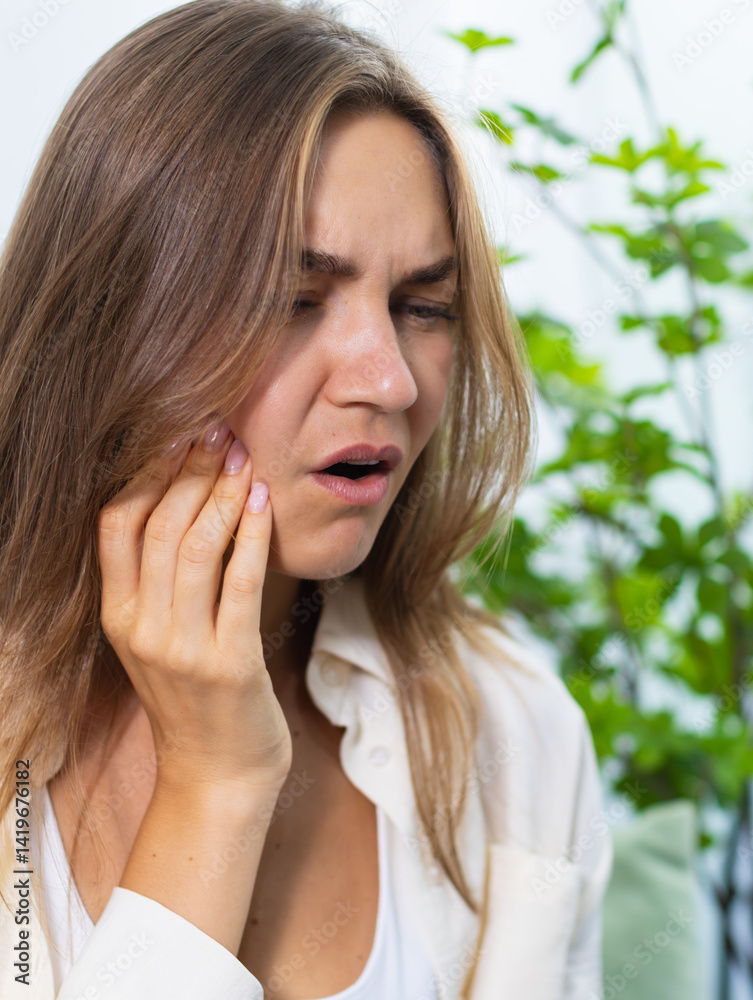 Young Caucasian Woman touching cheek with dental problem while sitting on couch at home, Unhappy, Unwell woman suffering from sensitive teeth, Woman having toothache at home. Dental health Concept. Young Caucasian Woman touching cheek with dental problem while sitting on couch at home, Unhappy, Unwell woman suffering from sensitive teeth, Woman having toothache at home. Dental health Concept.