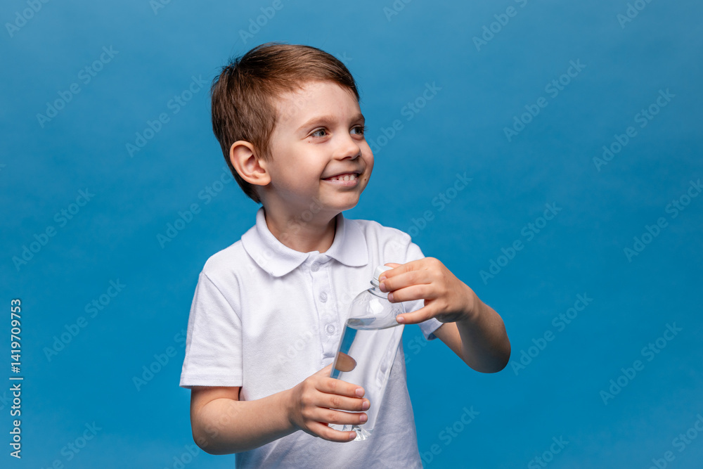 Happy little boy drinks water for health on a blue background. The child is opening a bottle of water. A kid with a plastic bottle. Children's activity and energy, generation Z. body hydration concept