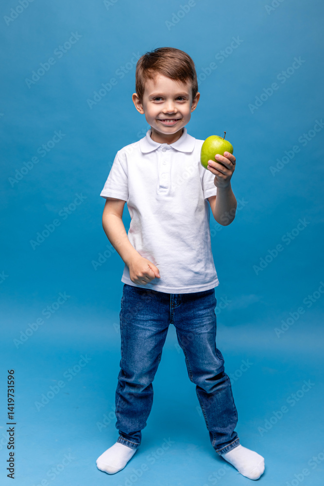 Happy little boy in white t-shirt holding green apple isolated on blue background. Proper nutrition. Child health. vegetarianism. High quality photo. Copy space