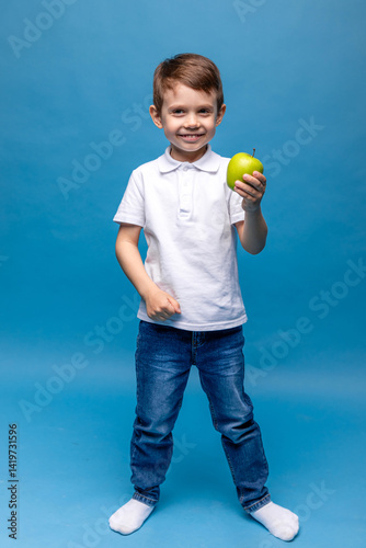 Obraz na płótnie Happy little boy in white t-shirt holding green apple isolated on blue background. Proper nutrition. Child health. vegetarianism. High quality photo. Copy space w salonie