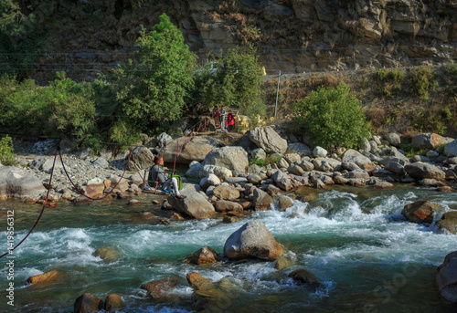 A tourist crossing a stream in a small makeshift mechanical ropeway in Tirthan Valley (Himachal Pradesh, India)