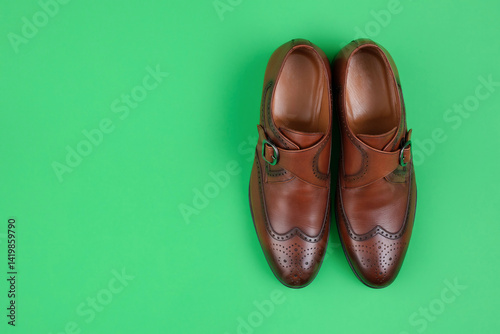Brown leather shoes on a green background. Top view, copy space