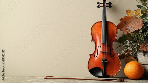 Elegant wooden violin with bow leaning against a wall next to a bouquet of autumn leaves and pumpkin on a neutral background, still life music instrument scene