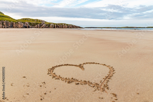 Ceannabeinne Beach shines under a clear summer sky. Crystal-clear waters, golden sand with a heart drawn on it, and lush green grass create a pristine and romantic coastal escape.

