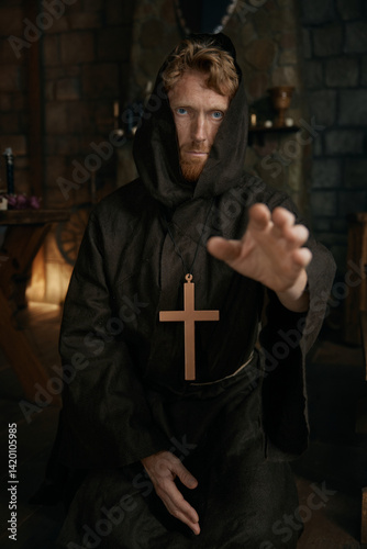 Portrait of friar wearing robe and golden cross reaching hand to camera