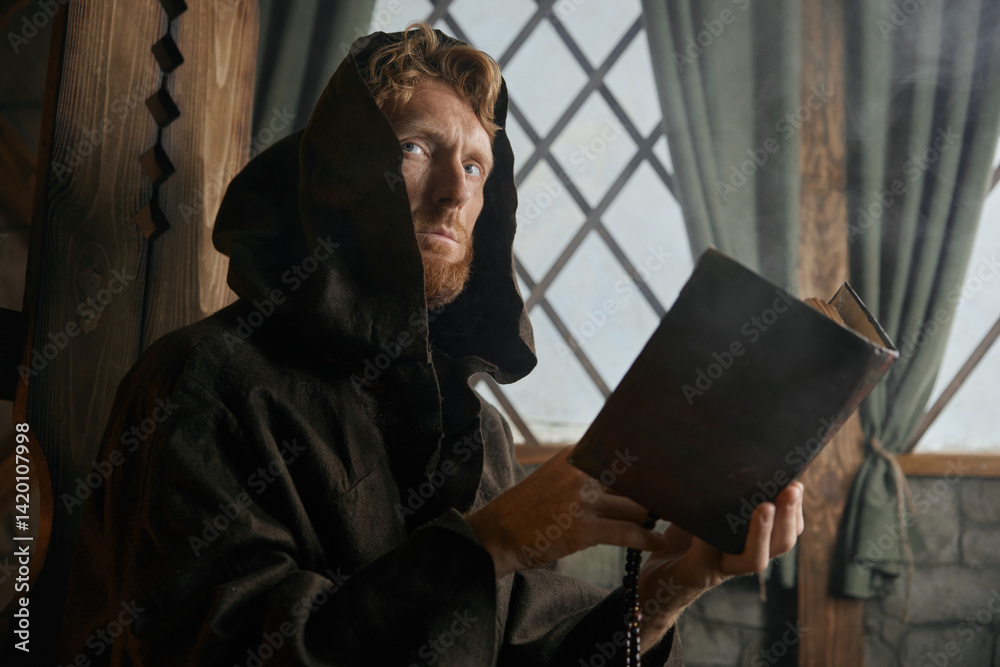 Old medieval monk reading sacred religious book praying with rosary beads in hand