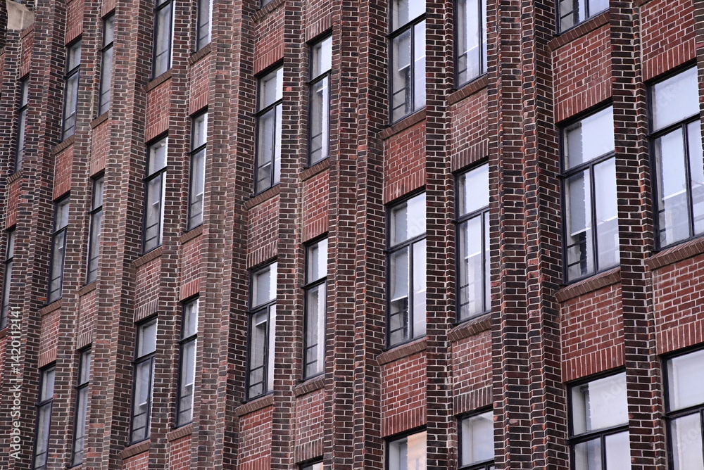 Fototapeta premium A building with a repetitive facade of red brick and evenly spaced windows. The image shows a tall urban structure.