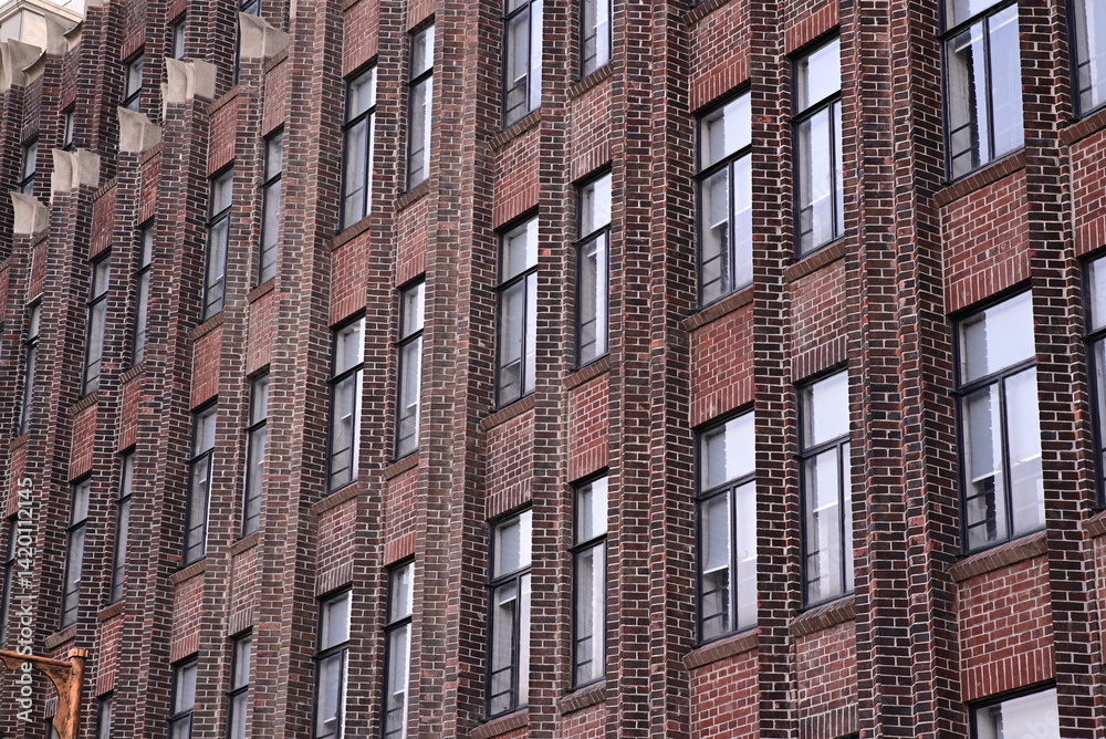 Obraz premium A building with a repetitive facade of red brick and evenly spaced windows. The image shows a tall urban structure.