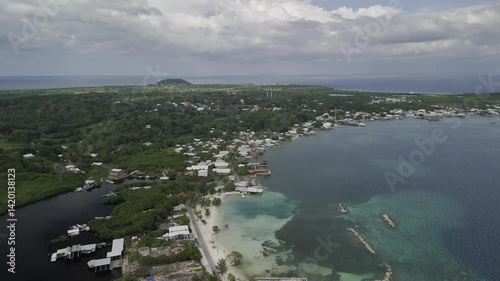 Drone flies backwards high over isthmus next to Chepes Beach in Utila, Honduras on partially cloudy afternoon
