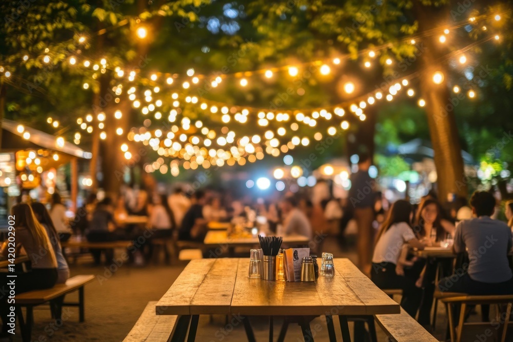 Outdoor dining at night, illuminated by string lights. Busy gathering of people enjoying an evening meal Outdoor dining at night, illuminated by string lights. Busy gathering of people enjoying an evening meal