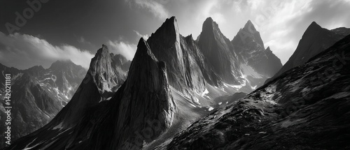 Majestic, rugged mountains tower dramatically against a cloudy sky in a stark black and white landscape.