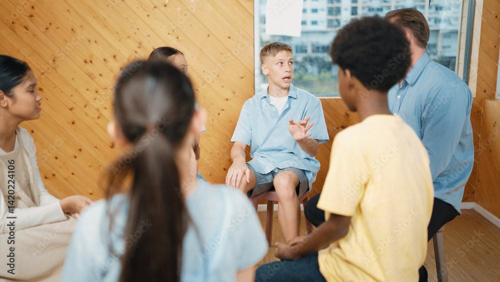 Fototapeta premium Attractive boy sharing experience during attend in group therapy. Highschool student talking about way to recovery stress while surrounded with multicultural friend listeing carefully. Edification.