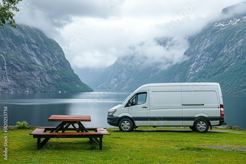 A green van is parked next to a picnic table by a lake. camper van parked at the green grass by lake with mountain background in cloudy day