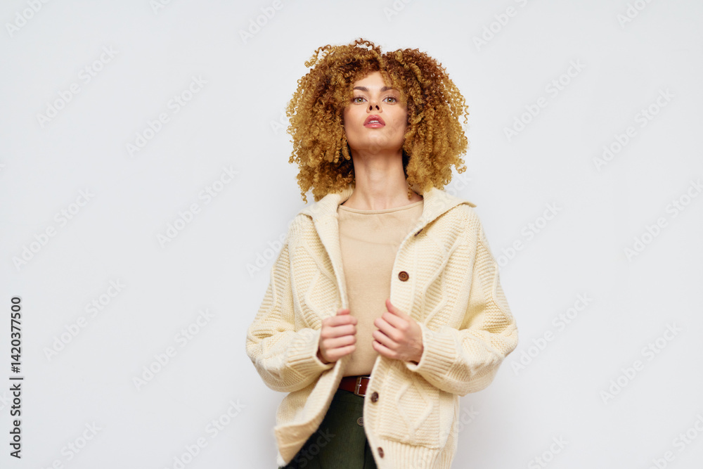 Fashionable woman in a cozy cream colored sweater against a plain white background, showcasing modern style and confidence through her expression and attire