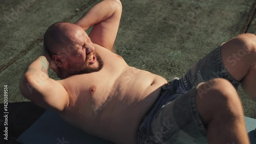 Fat man is trying to pump his abs outdoors, determined to lose weight and get back in shape. A motivated person does exercises outside and recuperates