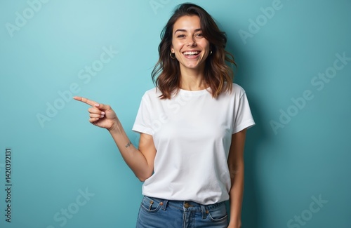 Young, beautiful, happy woman in white t-shirt points right with finger on blue background. Smiling female, copy space for advertising, mock up. Attractive caucasian girl shows on something someone.