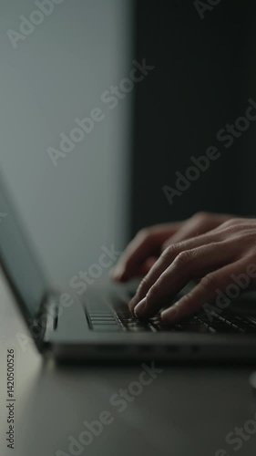 Vertical cropped shot of unrecognizable businessman working typing on laptop keyboard, focused work in professional setting in dark office environment by window, close-up. Shooting in slow motion.