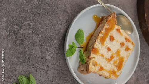 A single, tempting slice of caramelized molotov pudding, drizzled with rich caramel sauce and garnished with fresh mint leaves, presented on a round plate with a spoon, viewed from directly above.