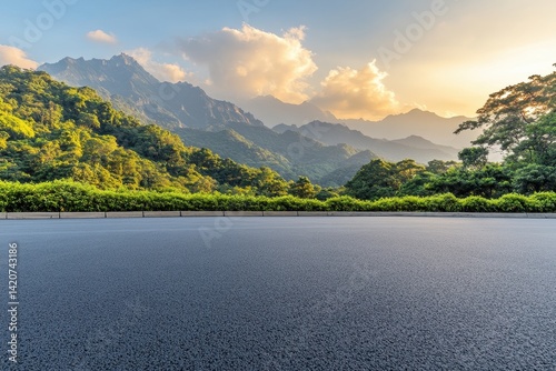 Empty asphalt road leading to a scenic mountain landscape at sunset. Lush greenery surrounds the road, nestled in valleys between towering peaks.  Golden sunlight illuminates the scene