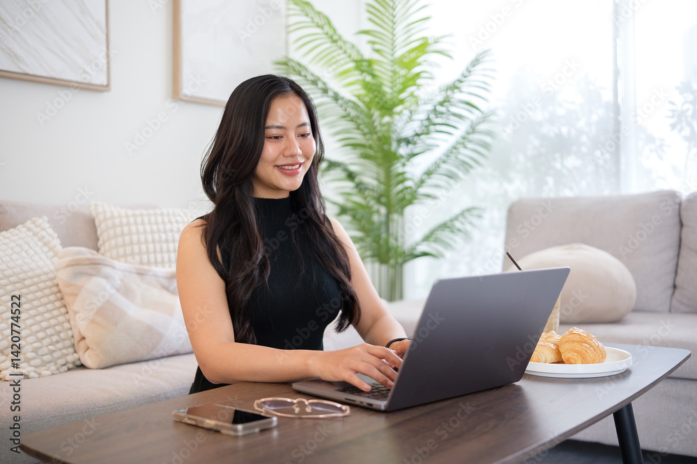 Young woman using laptop in the living room with coffee and croissant, enjoying a relaxed morning. Young woman using laptop in the living room with coffee and croissant, enjoying a relaxed morning.