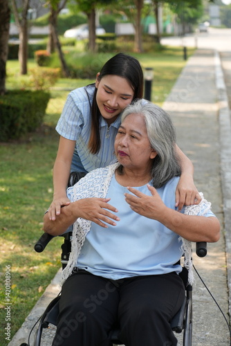 Two women, the daughter pushing a stroller with her elderly mother, walk in the garden and chat happily.