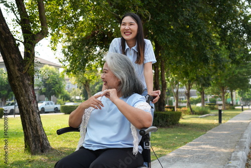 Two women, the daughter pushing a stroller with her elderly mother, walk in the garden and chat happily.