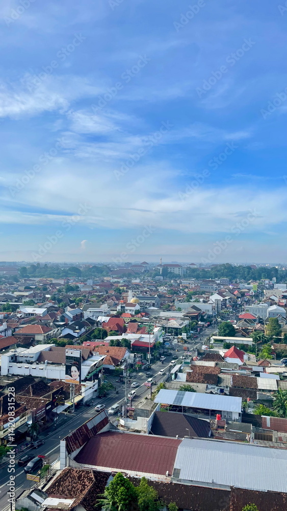 Naklejka premium Aerial view of Solo city with traditional red-roofed houses, modern buildings, and clear morning skies blending into the distant horizon.