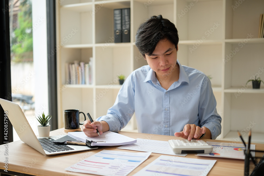 Businessman calculating business figures while reviewing paperwork at office desk.