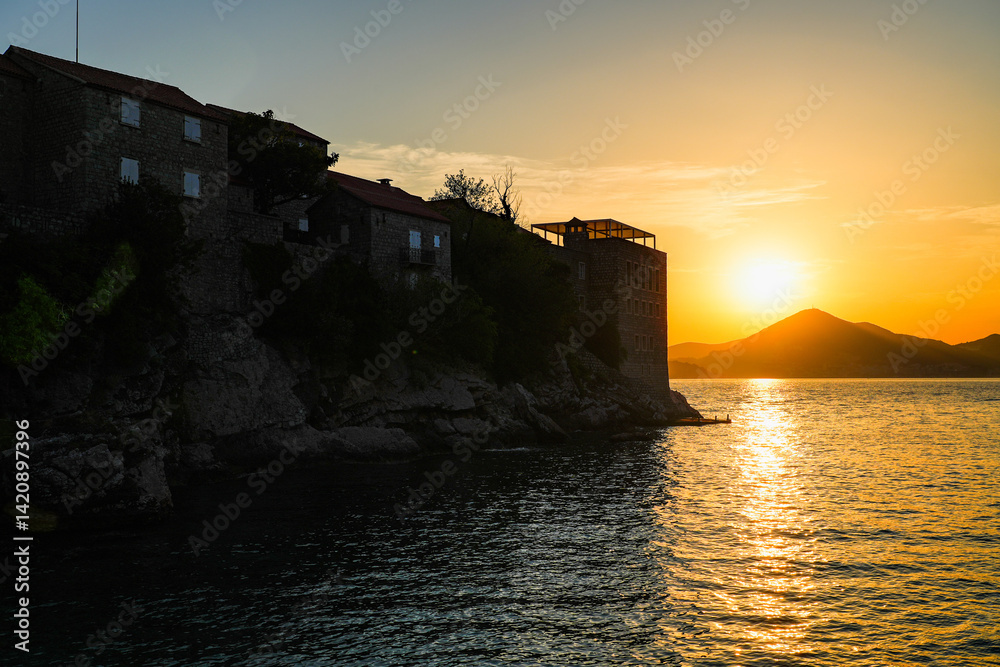 Sunset behind Sveti Stefan, a medieval village located on a small island connected to the mainland by a narrow tombolo (sandy isthmus) in the bay of Budva along the Adriatic Coast, Montenegro