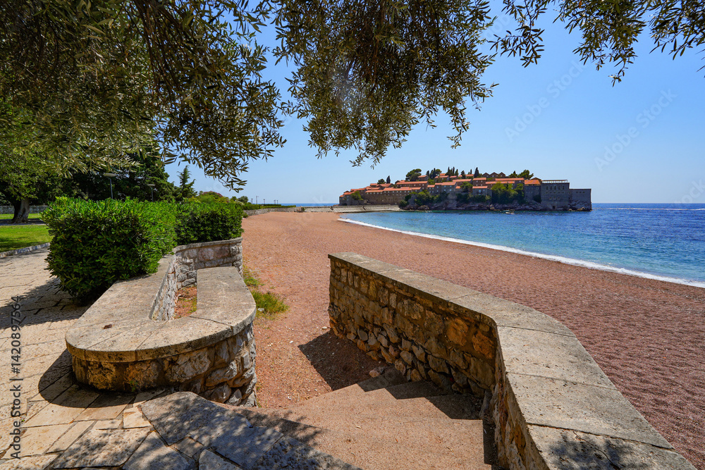 Beach of Sveti Stefan, a medieval village located on a small island connected to the mainland by a narrow tombolo (sandy isthmus) in the bay of Budva along the Adriatic Coast, Montenegro