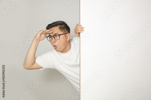 Young men peeking from behind wall with curious expression